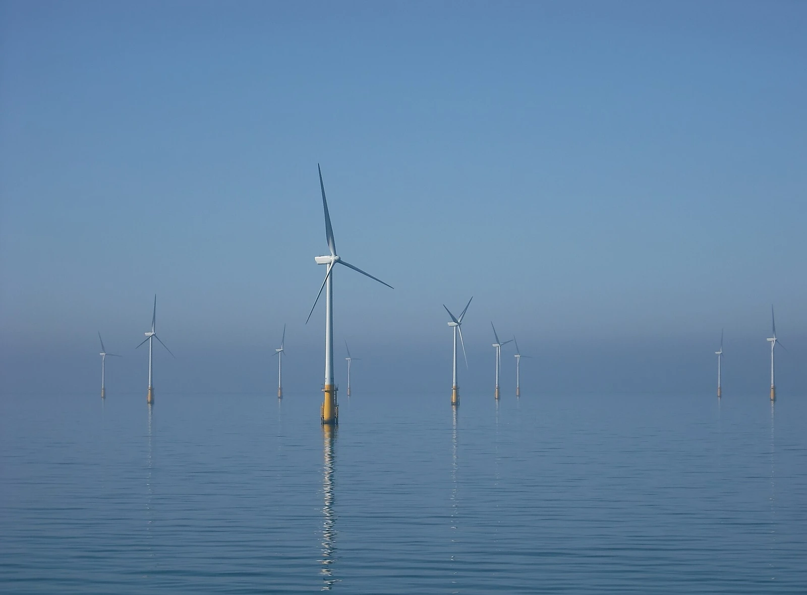 Offshore wind turbines standing in calm sea water, fading into haze toward the horizon